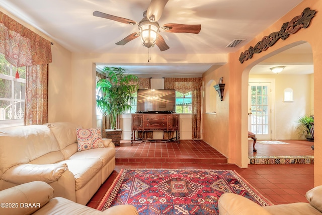 living area with ceiling fan, tile patterned flooring, visible vents, and arched walkways