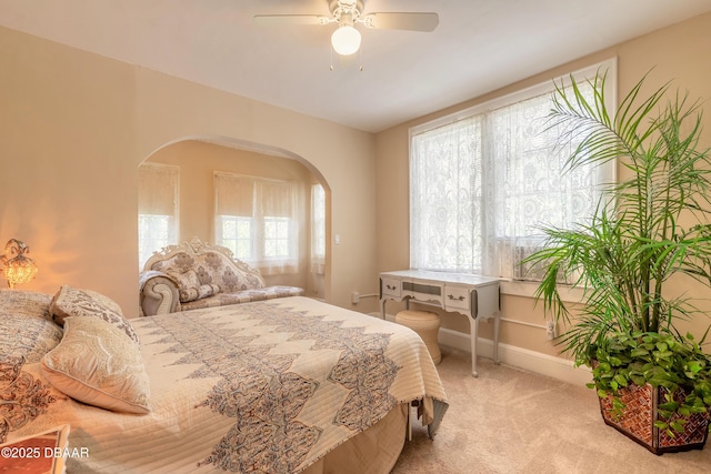 bedroom featuring light carpet, ceiling fan, arched walkways, and baseboards