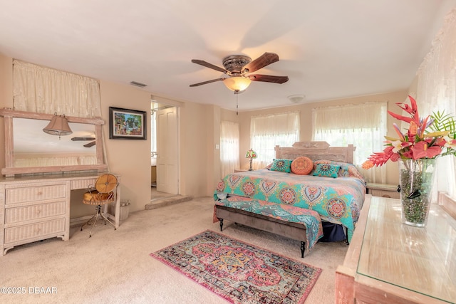 bedroom featuring light carpet, built in desk, visible vents, and a ceiling fan