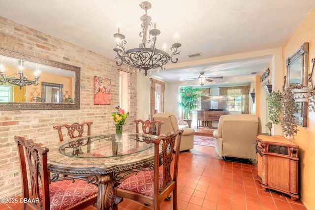 dining space featuring light tile patterned floors, visible vents, brick wall, and ceiling fan with notable chandelier