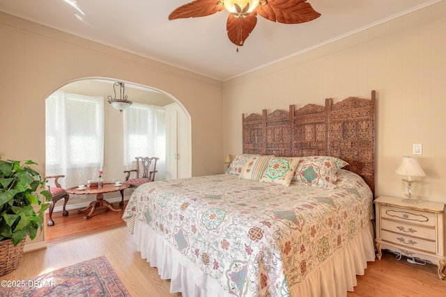 bedroom with arched walkways, crown molding, and light wood-style flooring