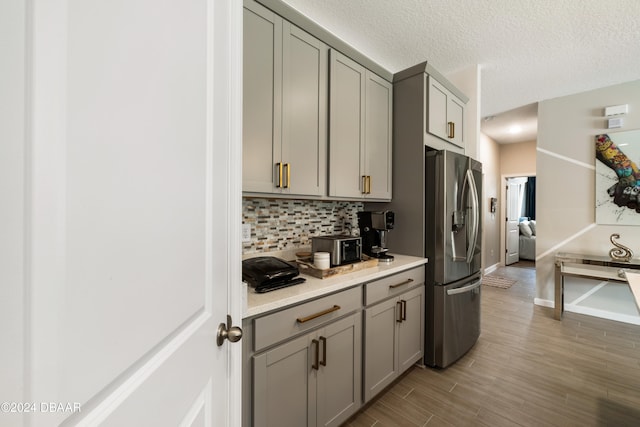 kitchen featuring light hardwood / wood-style floors, decorative backsplash, a textured ceiling, gray cabinets, and stainless steel fridge