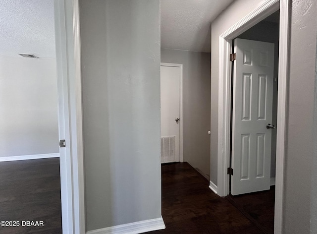 corridor featuring baseboards, dark wood-style floors, visible vents, and a textured ceiling