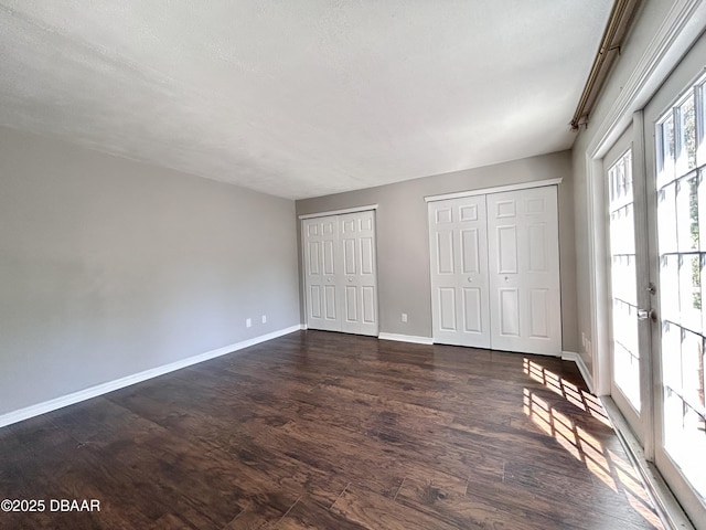 unfurnished bedroom featuring french doors, baseboards, two closets, and dark wood finished floors