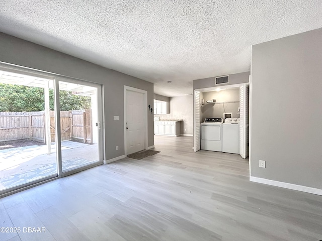 unfurnished living room featuring visible vents, washer and dryer, a textured ceiling, wood finished floors, and baseboards