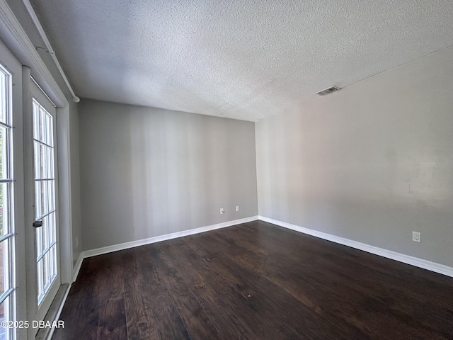 spare room featuring dark wood finished floors, baseboards, visible vents, and a textured ceiling