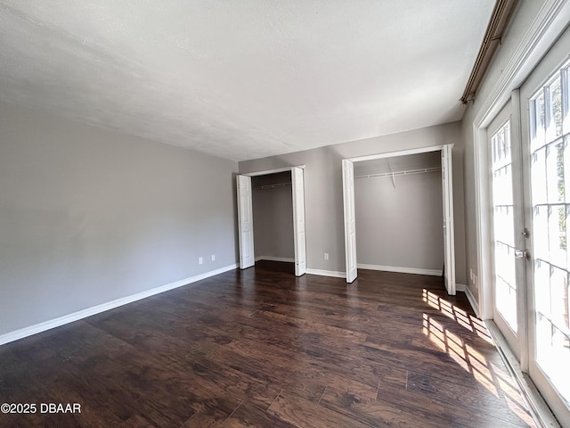 unfurnished bedroom featuring dark wood finished floors, french doors, baseboards, and multiple closets