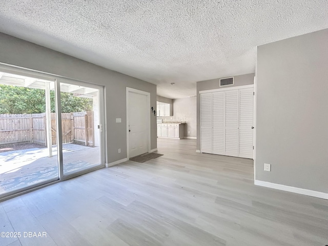 unfurnished living room with visible vents, a textured ceiling, light wood-type flooring, and baseboards