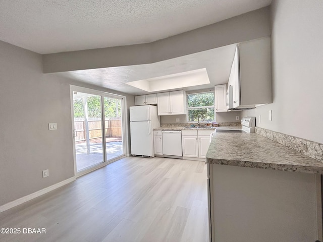 kitchen featuring baseboards, light wood-type flooring, a wealth of natural light, white appliances, and a raised ceiling