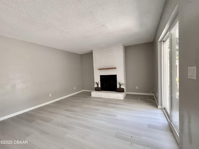 unfurnished living room featuring a brick fireplace, baseboards, and light wood finished floors