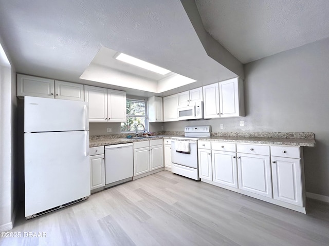 kitchen with white appliances, light wood finished floors, a tray ceiling, a sink, and white cabinets