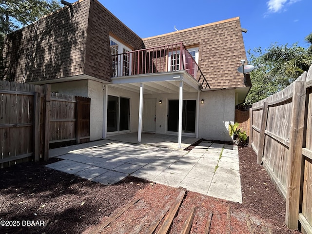 back of property with a shingled roof, stucco siding, mansard roof, a balcony, and a fenced backyard