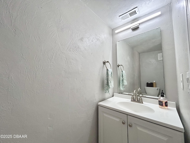 bathroom featuring vanity, a textured wall, visible vents, and a textured ceiling