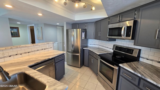 kitchen with light tile patterned floors, decorative backsplash, crown molding, appliances with stainless steel finishes, and a tray ceiling