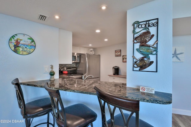 2625 S Atlantic Ave Unit 25Nw, Daytona Beach Shores, FL 32118 - kitchen with stainless steel appliances, white cabinetry, a peninsula, wood finished floors, and a breakfast bar area