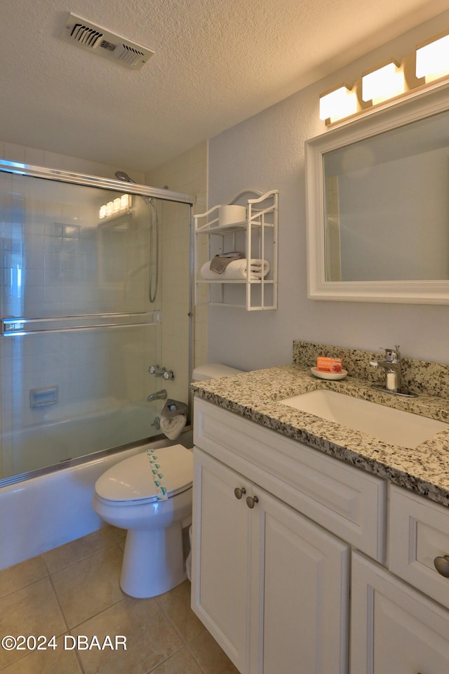 full bathroom featuring a textured ceiling, vanity, bath / shower combo with glass door, tile patterned floors, and toilet