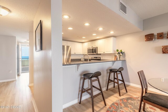5300 S Atlantic Ave Unit 1-603, New Smyrna Beach, FL 32169 - kitchen featuring stainless steel appliances, a breakfast bar area, a textured ceiling, light wood-style flooring, and white cabinets