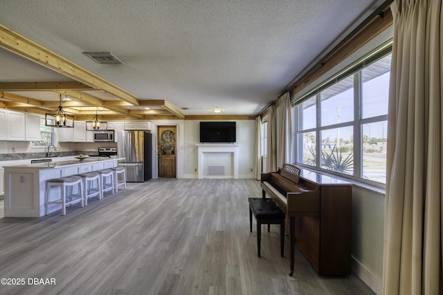 living room featuring sink, a textured ceiling, beamed ceiling, and light wood-type flooring