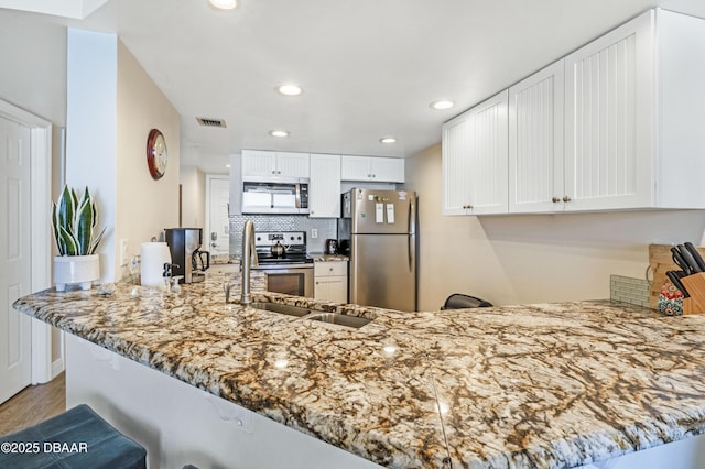 4453 S Atlantic Ave Unit 502, Port Orange, FL 32127 - kitchen with visible vents, a peninsula, light stone countertops, white cabinetry, and appliances with stainless steel finishes