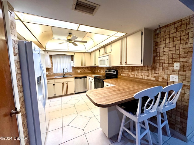 kitchen featuring white appliances, cream cabinets, light tile patterned floors, kitchen peninsula, and a breakfast bar area