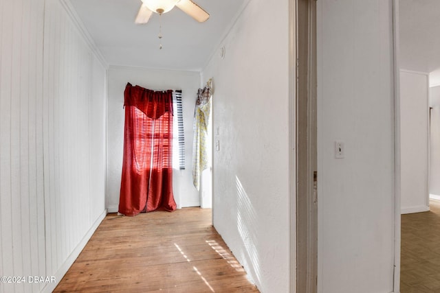 hall featuring light wood-type flooring, wooden walls, and ornamental molding