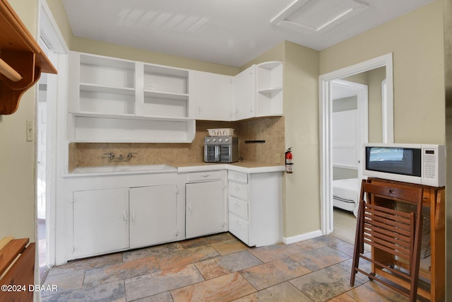 kitchen with decorative backsplash, sink, white cabinets, and a baseboard heating unit