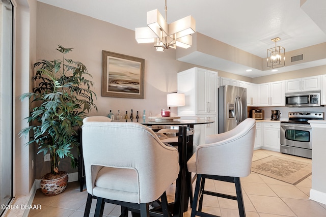 kitchen with stainless steel appliances, white cabinetry, light tile patterned floors, pendant lighting, and a chandelier