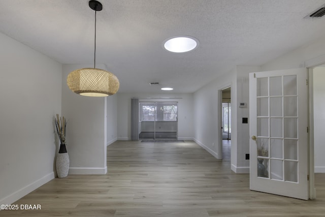 hallway with a textured ceiling, baseboards, visible vents, and wood finished floors