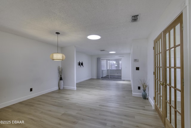 interior space featuring a textured ceiling, visible vents, baseboards, and light wood finished floors