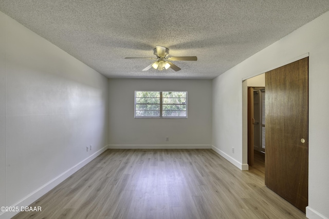 empty room with baseboards, a ceiling fan, light wood finished floors, and a textured ceiling