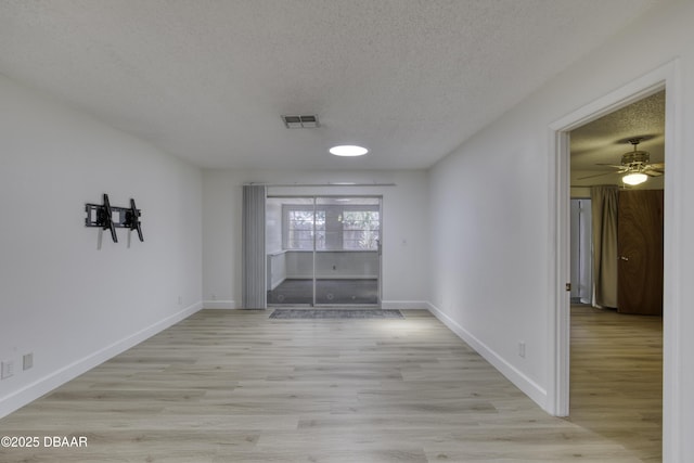 corridor with baseboards, light wood-style flooring, a textured ceiling, and visible vents
