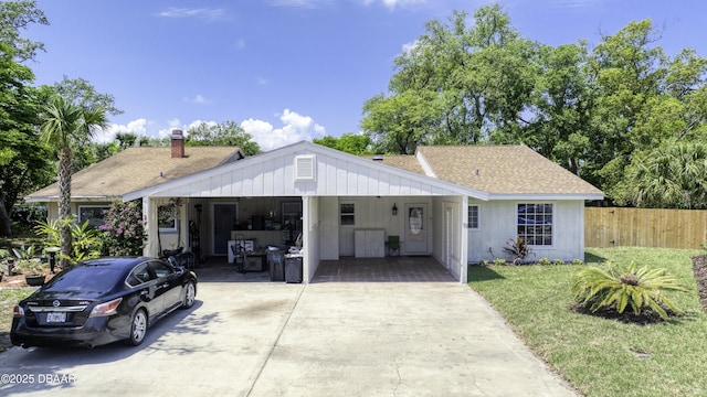 view of front facade featuring a front lawn, fence, roof with shingles, an attached carport, and concrete driveway