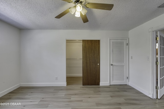 unfurnished bedroom featuring multiple closets, baseboards, a textured ceiling, a ceiling fan, and light wood finished floors