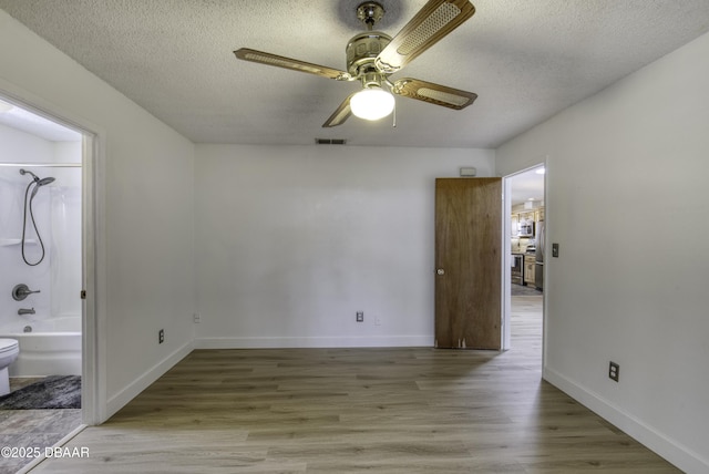 unfurnished bedroom featuring visible vents, baseboards, a textured ceiling, and wood finished floors