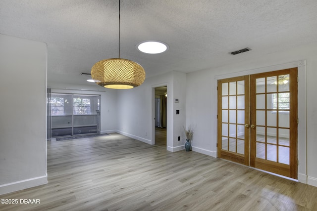 unfurnished dining area featuring a textured ceiling, visible vents, french doors, and wood finished floors