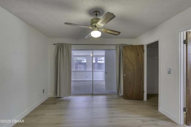 unfurnished bedroom with baseboards, a textured ceiling, a walk in closet, and light wood-type flooring