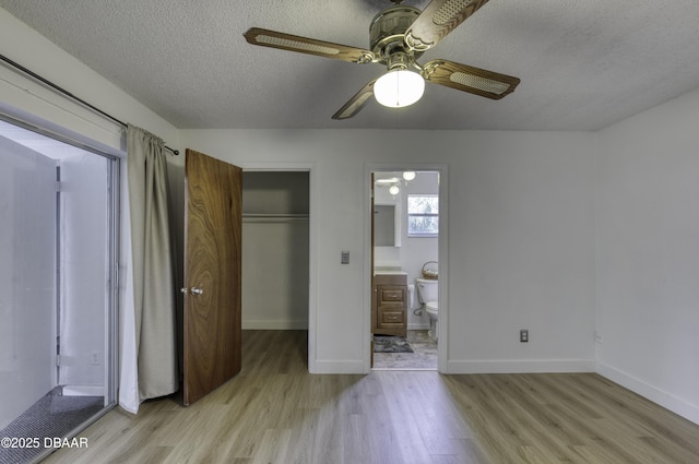 unfurnished bedroom featuring a textured ceiling, a walk in closet, light wood finished floors, and a closet