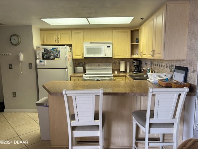 kitchen with kitchen peninsula, white appliances, sink, and a breakfast bar