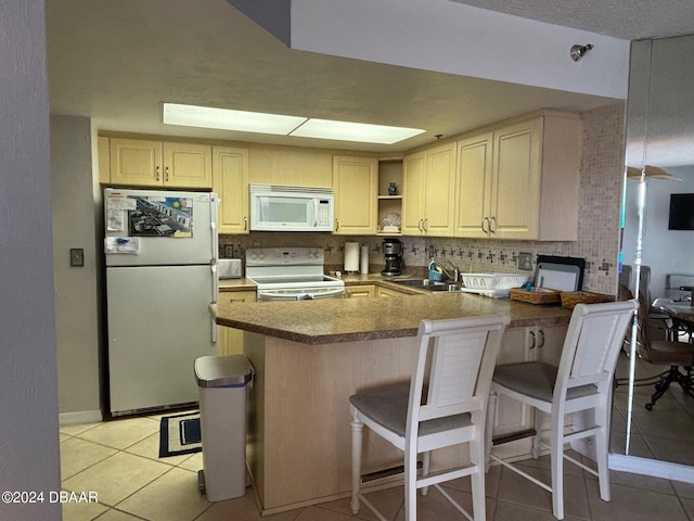 kitchen featuring kitchen peninsula, a kitchen breakfast bar, white appliances, and light tile patterned floors