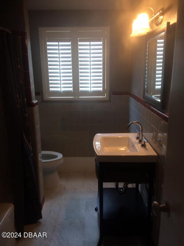 500 S Beach St Unit B-2, Daytona Beach, FL 32114 - bathroom with tile walls, walk in shower, sink, tile patterned flooring, and toilet