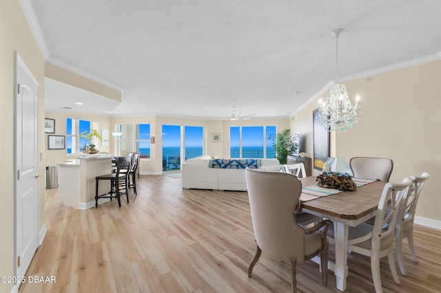 dining area featuring ceiling fan with notable chandelier, a water view, light hardwood / wood-style flooring, and crown molding