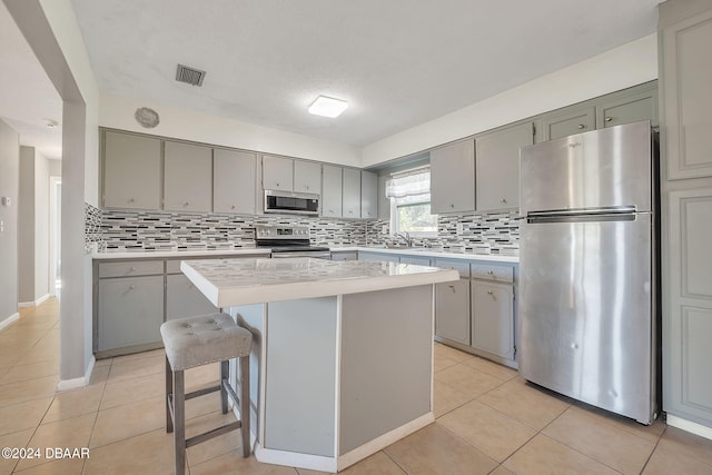 kitchen featuring tasteful backsplash, light tile patterned flooring, a kitchen island, appliances with stainless steel finishes, and a kitchen bar