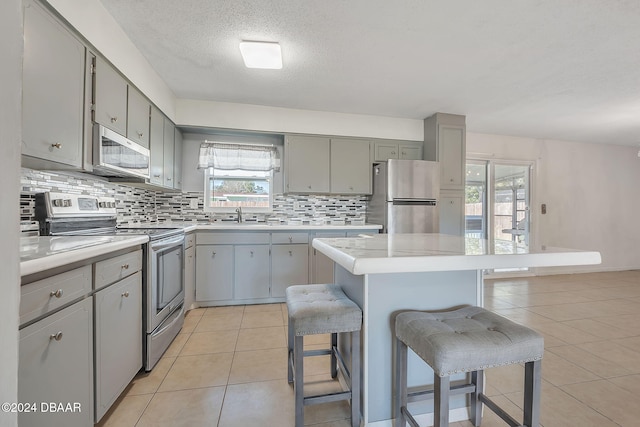 kitchen featuring light tile patterned flooring, stainless steel appliances, a kitchen bar, gray cabinets, and a center island