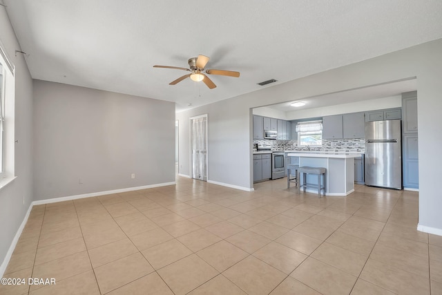 unfurnished living room with a textured ceiling, ceiling fan, and light tile patterned floors