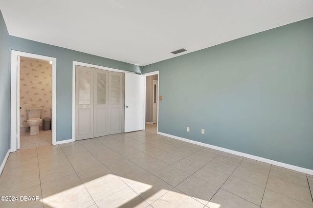 unfurnished bedroom featuring ensuite bathroom, light tile patterned flooring, and a closet