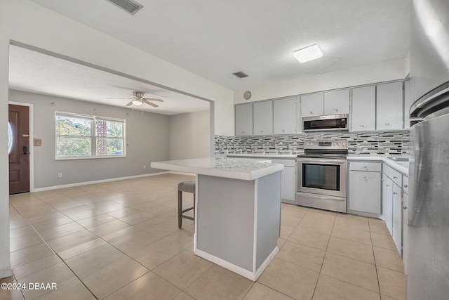 kitchen featuring stainless steel appliances, a breakfast bar area, light tile patterned floors, ceiling fan, and backsplash