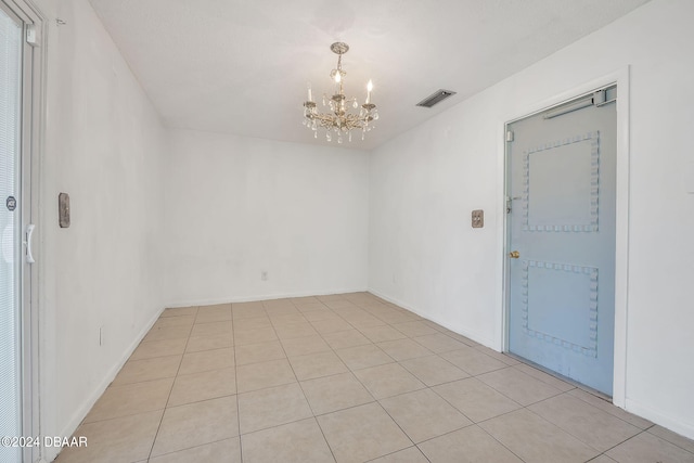 empty room with light tile patterned floors and a notable chandelier