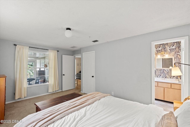 bedroom with visible vents, light colored carpet, and ensuite bath