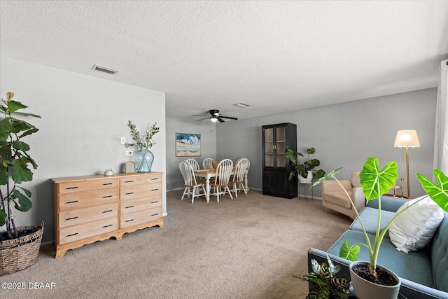 carpeted living room featuring visible vents, ceiling fan, and a textured ceiling