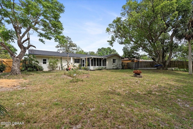 rear view of house with a fire pit, a fenced backyard, a sunroom, and a lawn